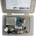 An electronics kit in a clear plastic storage case, containing a breadboard, various electronic components in plastic bags, and wires, with a handwritten label on the inside lid.